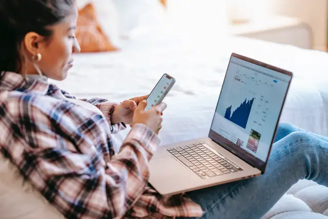 Alternatives to the Stock Market: Where Else to Invest Your Money 2 womаn looking at her phone with a laptop on her lap