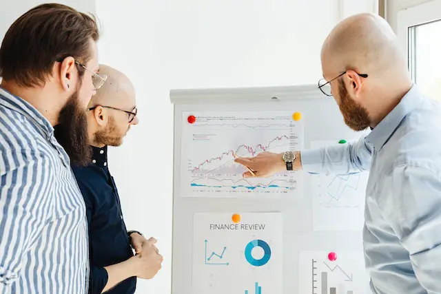 three man in front of a stock trading charts