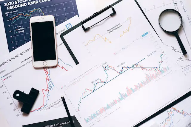 stock charts on paper with a cell phone and magnifying glass on top