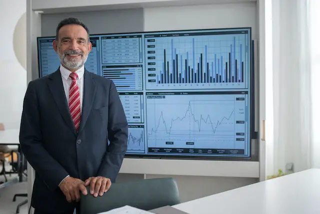 man standing in front of a large monitor with stock charts on it