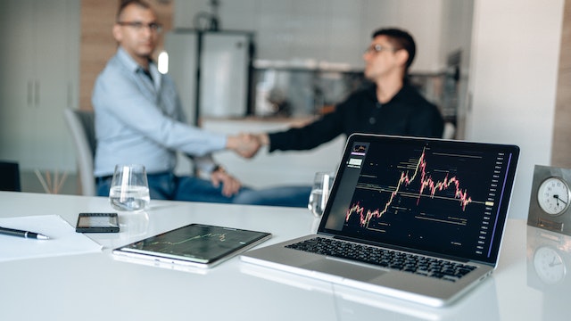 stock trading chart on a laptop with two man shaking hand in the background