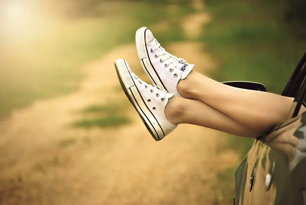 Crossed legs with sneakers sticking out from a car window 