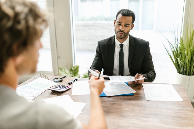 two man at a desk exchanging papers