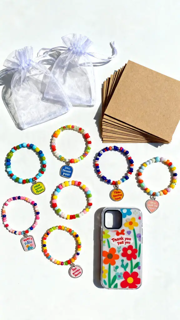 12 Ways To Make Money As A 14 Year Old Online 3 A flat-lay display of handmade beaded bracelets and phone charms next to packaging bags and thank-you cards on a white surface.